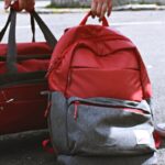 Two travelers holding red bags on a street, symbolizing travel and exploration.