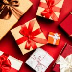 Top view of beautifully wrapped holiday gifts with red and brown ribbons on a vibrant red background.